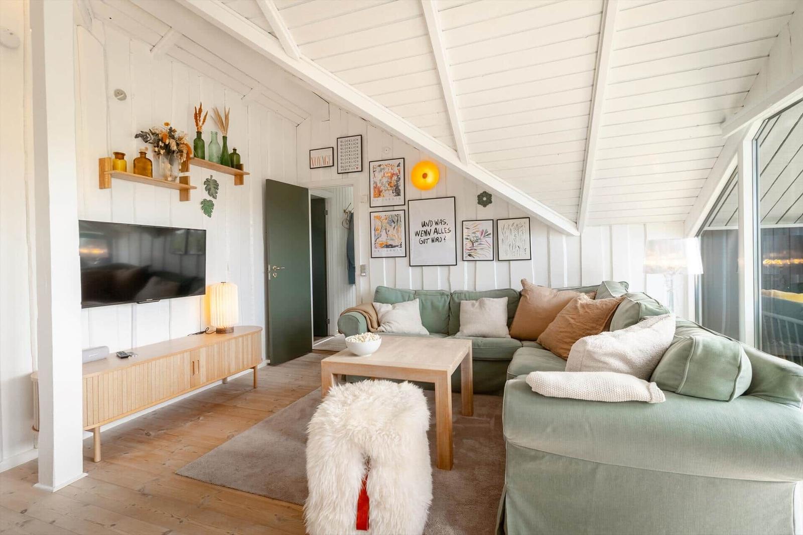 Wohnzimmer mit Sofa, Fernseher und Holzmöbeln unter schrägem Dach.