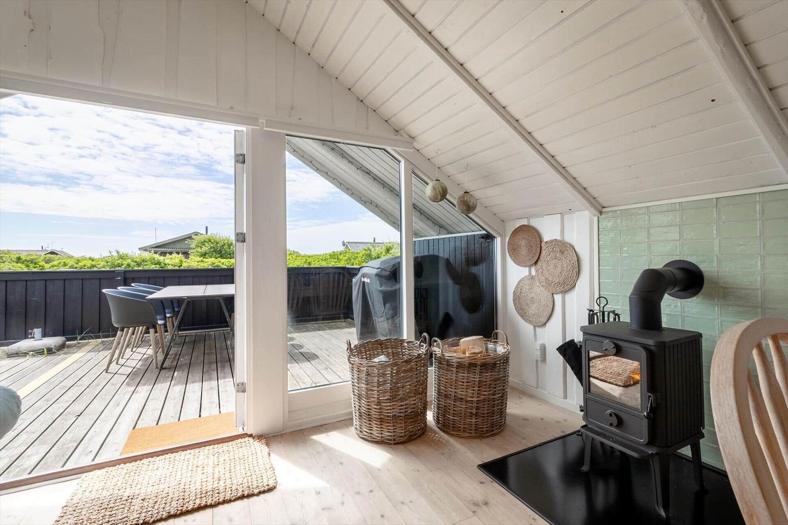 Raum mit Kaminofen, Holzdielen und Terrasse mit Tisch und Stühlen.