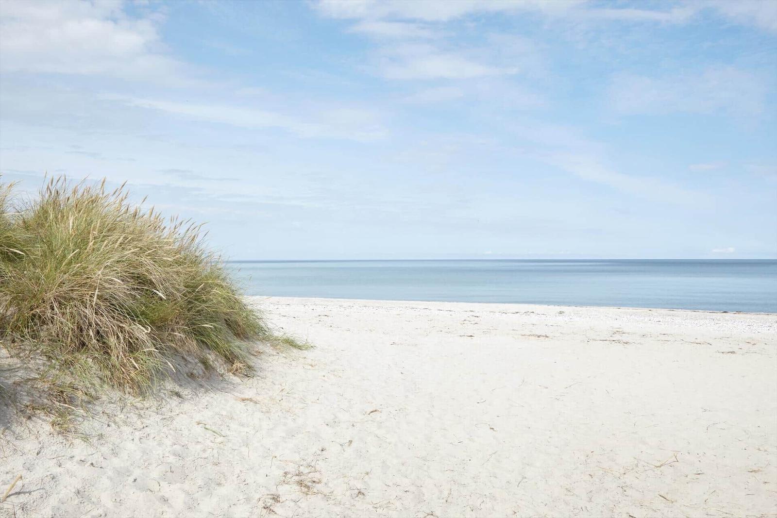 Weißer Sandstrand mit Dünen und ruhigem Meer unter blauem Himmel.