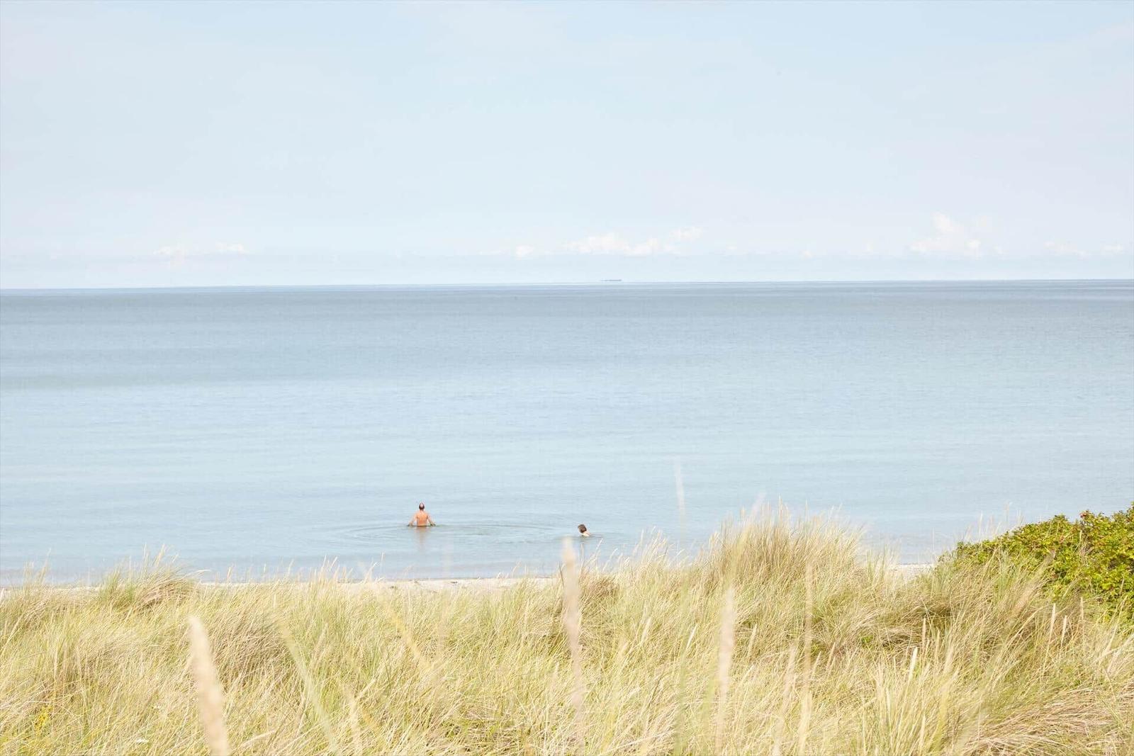 Zwei Personen schwimmen im Meer, umgeben von Dünen und Horizont.