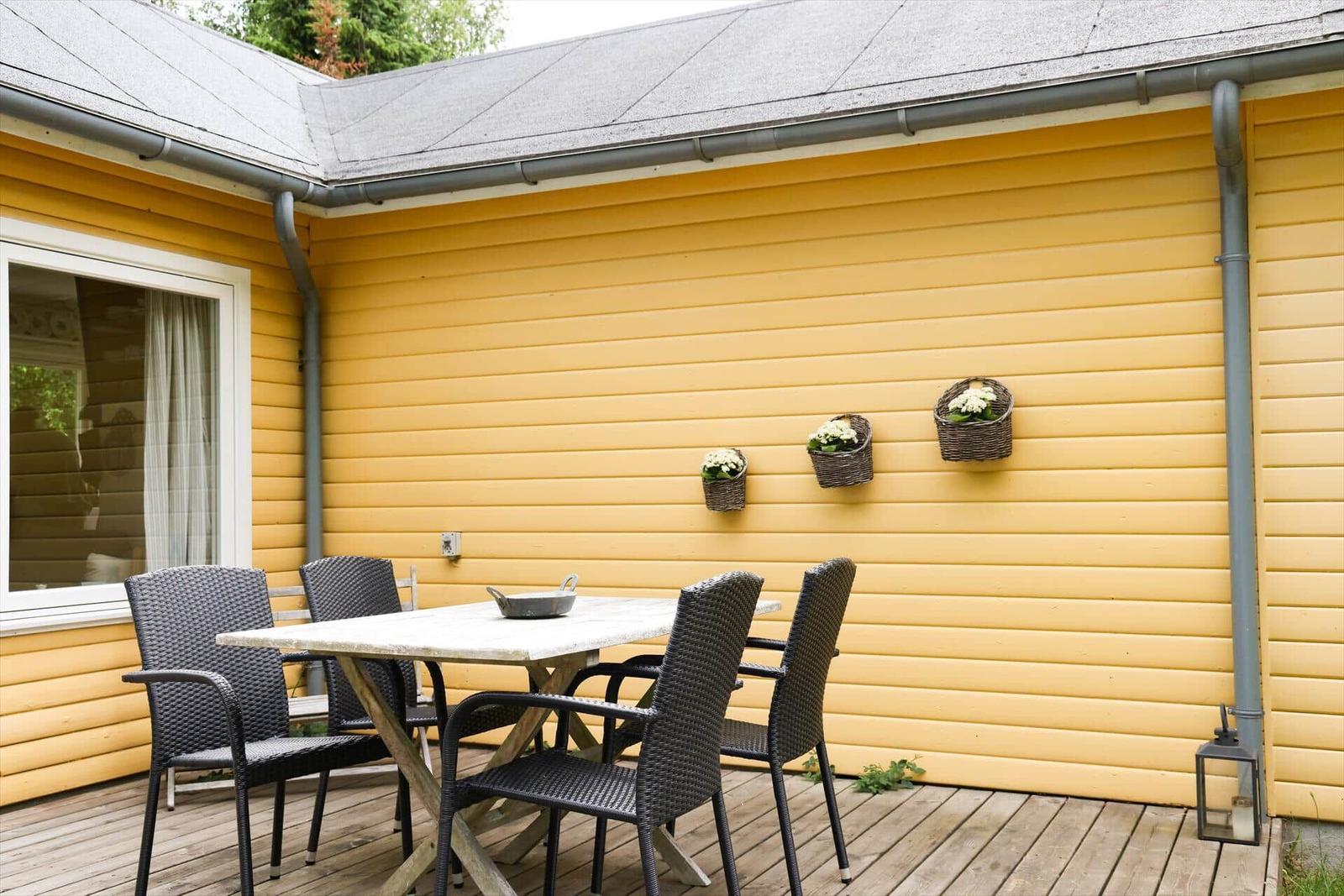 Terrasse mit Tisch und Stühlen an gelbem Haus mit Blumenkörben.