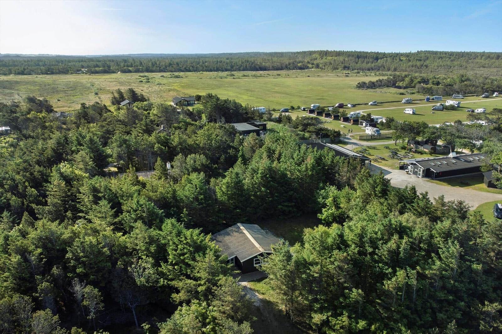 Aerial view of a campground with cabins, trees, and open fields under clear skies.