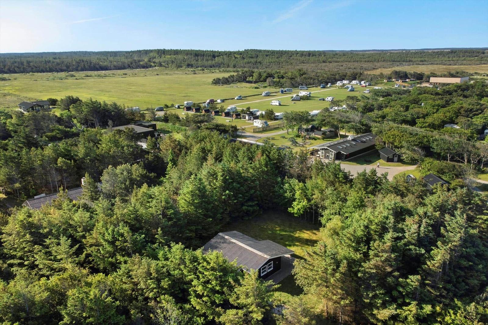 Liegenschaft mit Wald, Grünflächen und Campingplätzen unter blauem Himmel.
