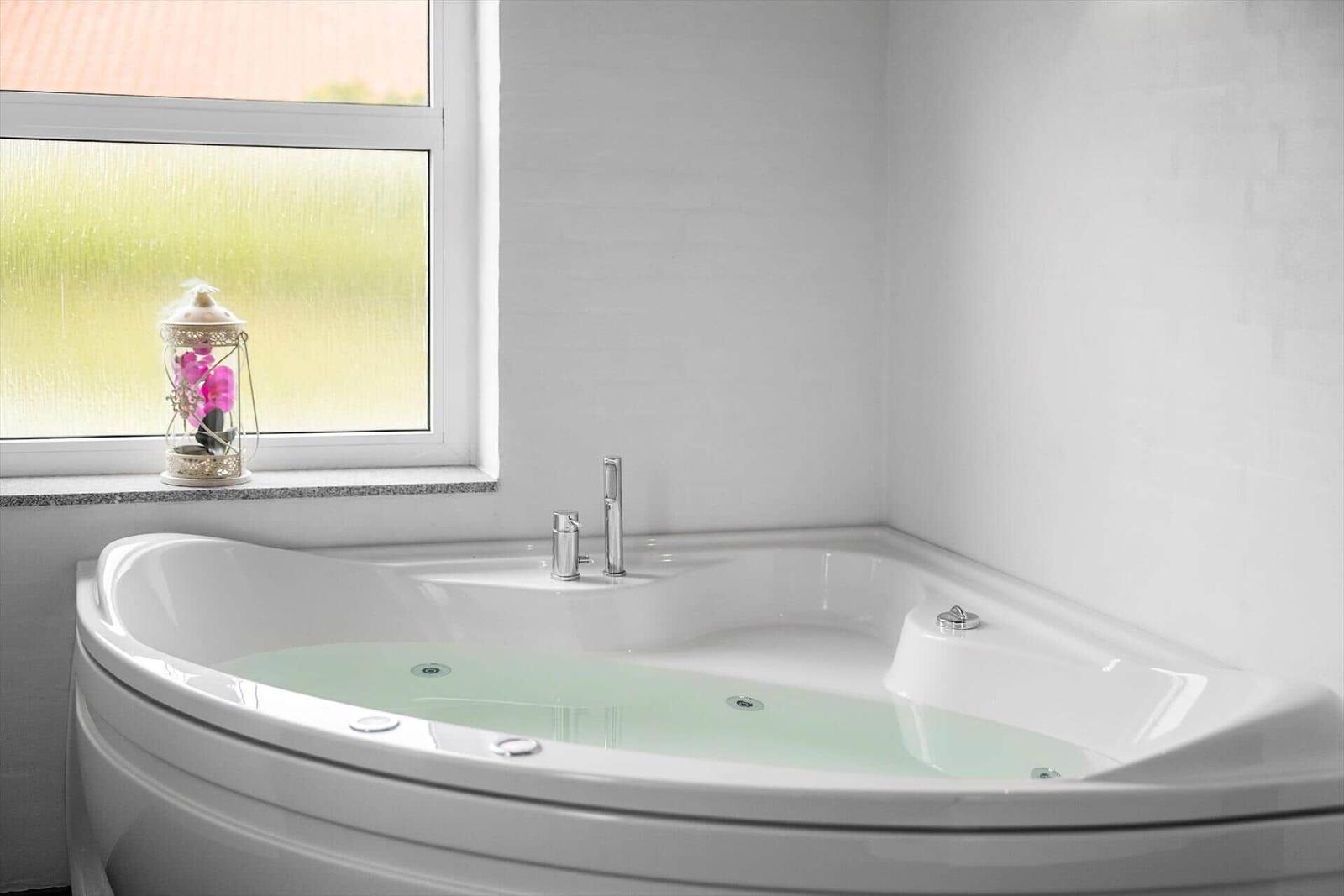 Eckbadewanne mit Wasser, Fenster und Laterne auf Sims