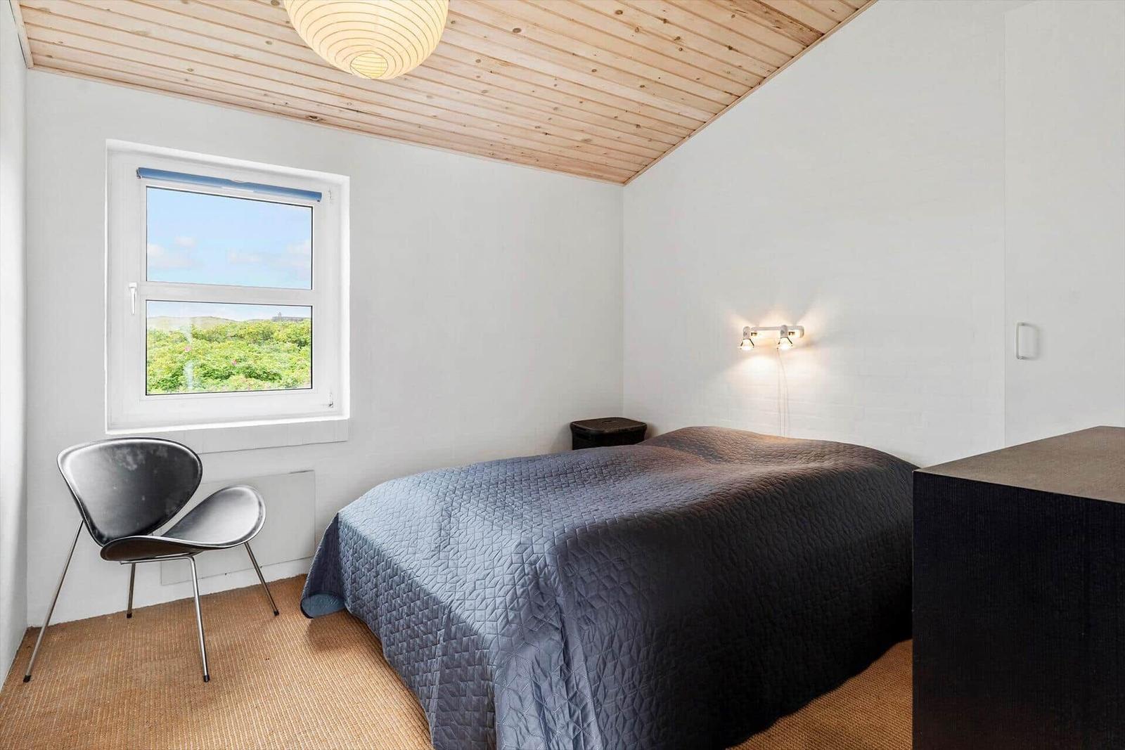 Schlafzimmer mit Bett, Stuhl und Fenster mit Blick auf Grün.