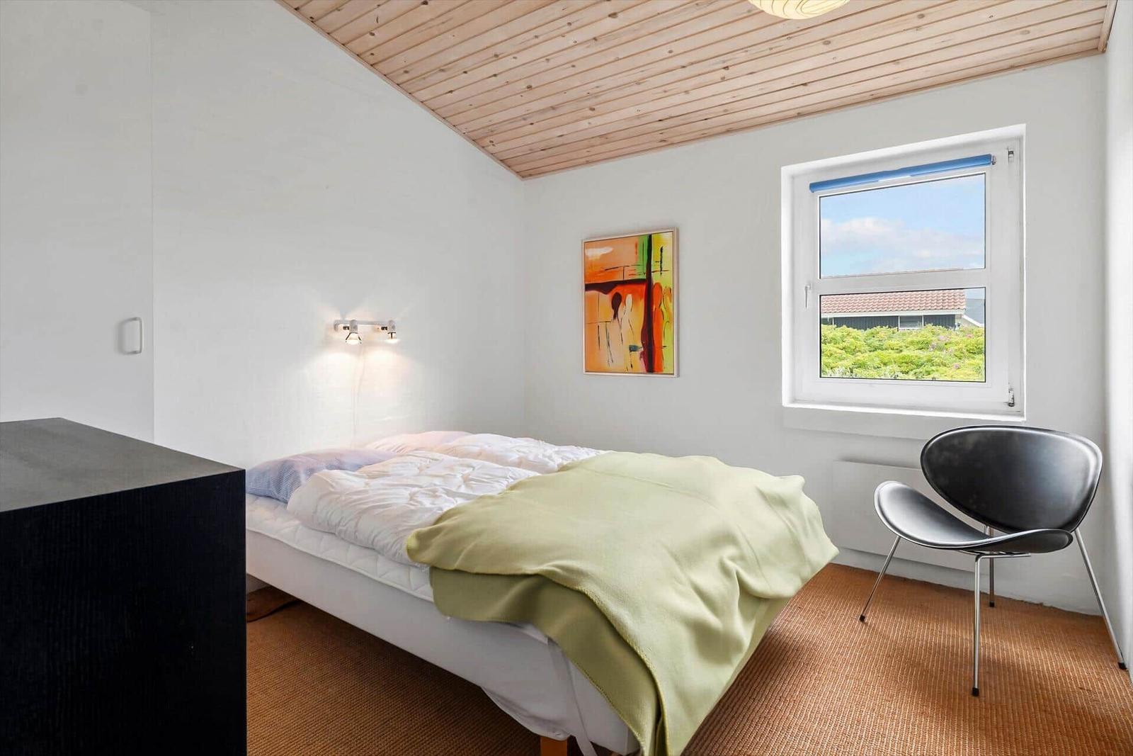 Schlafzimmer mit Bett, Stuhl und Fensterblick auf Grünflächen.