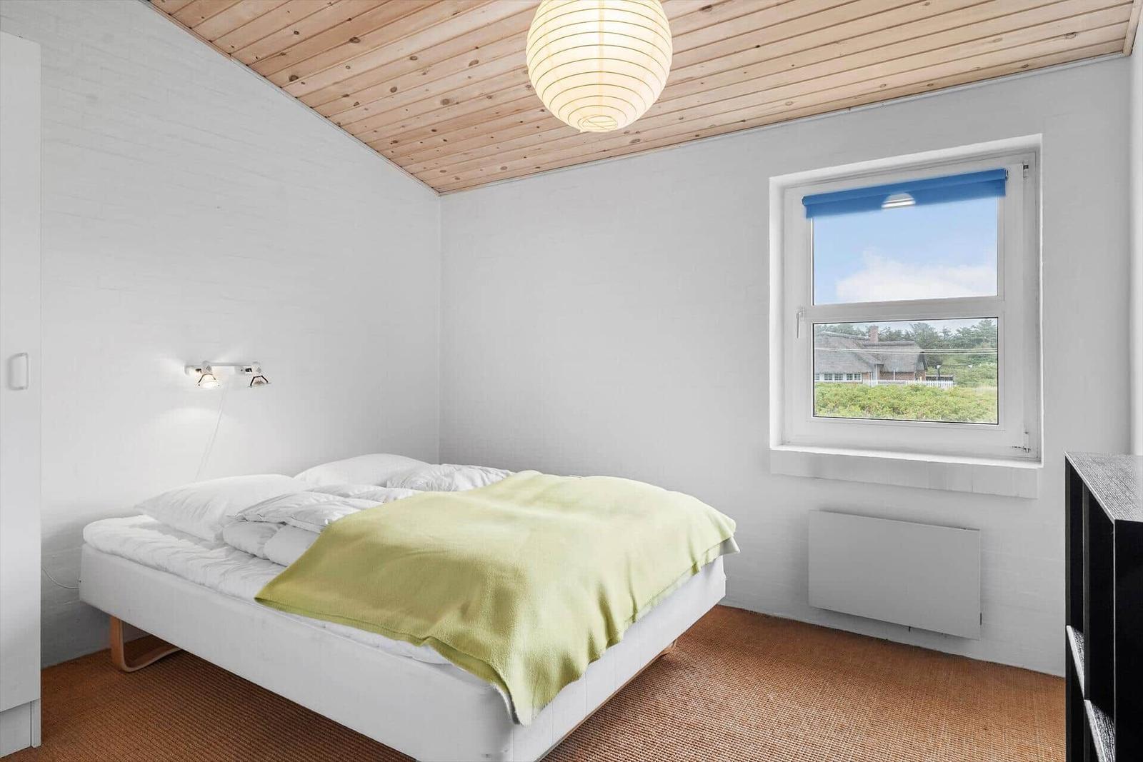 Schlafzimmer mit Bett, Fenster und Holzdecke.