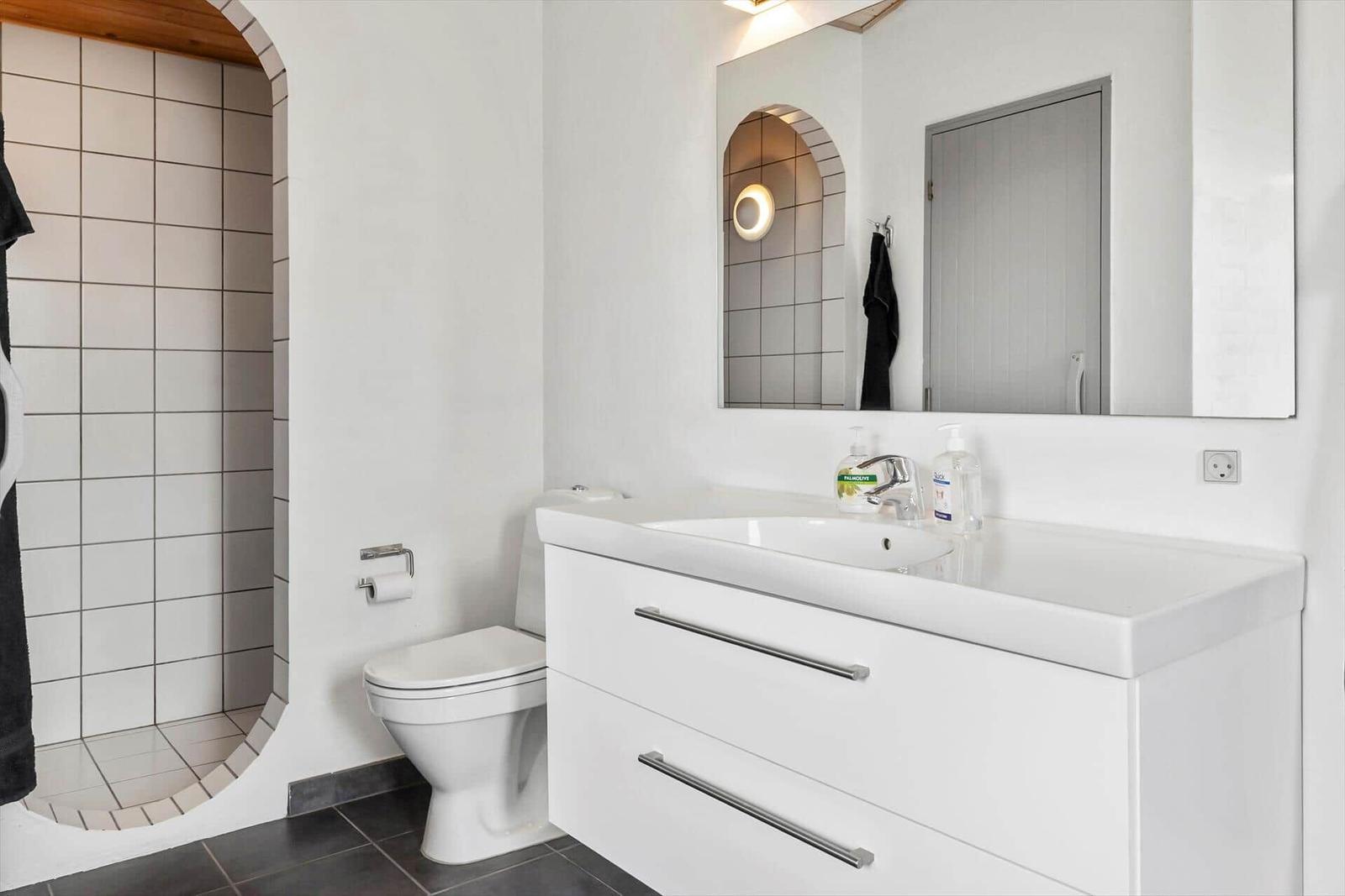 Badezimmer mit Waschtisch, Toilette und Dusche mit Bogenöffnung.