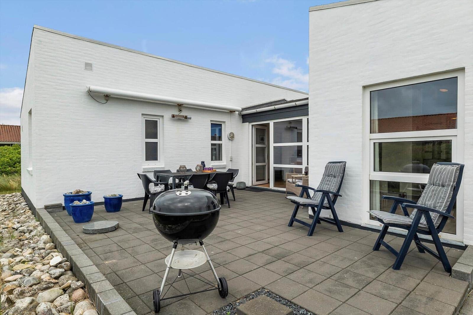 Terrasse mit Grill, Tisch, Stühlen und Sitzgelegenheiten vor weißem Haus