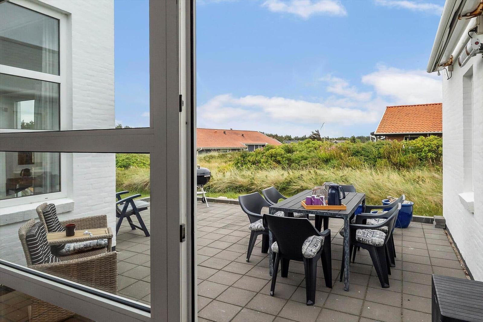 Terrasse mit Tisch, Stühlen und Grill. Blick auf Grasland und Häuser.