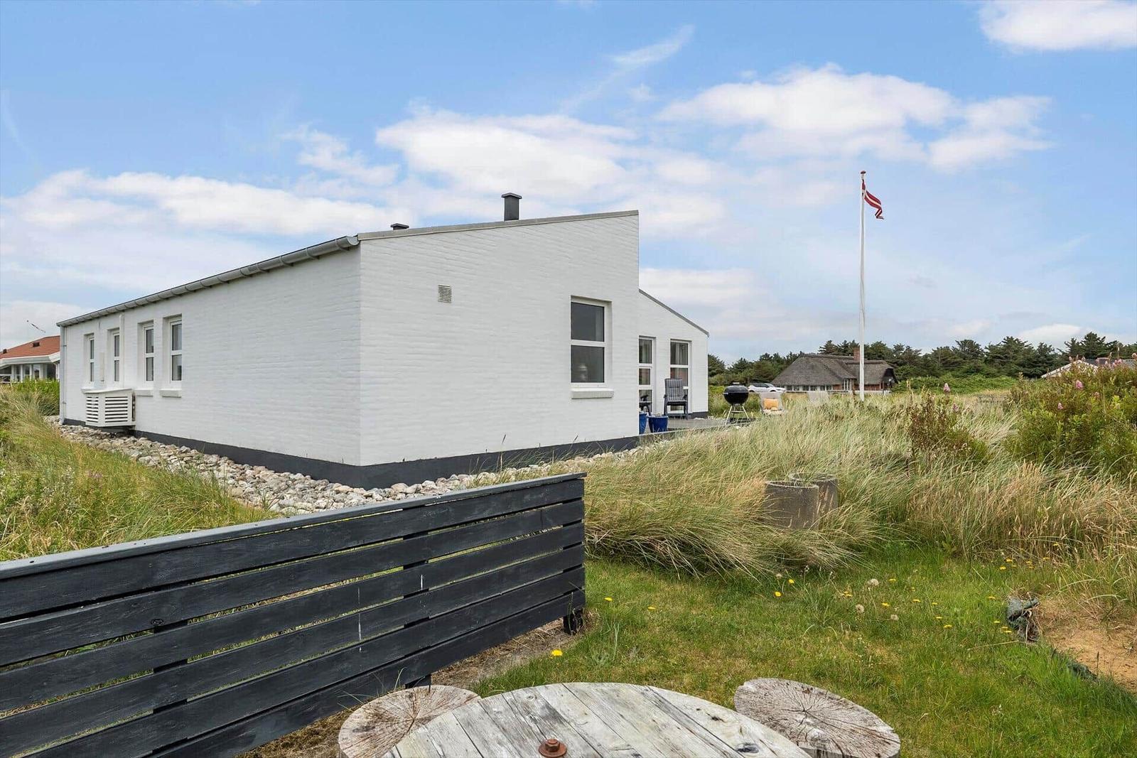 Weiße Ferienhaus mit Terrasse, Grill und Flagge im Grasland.
