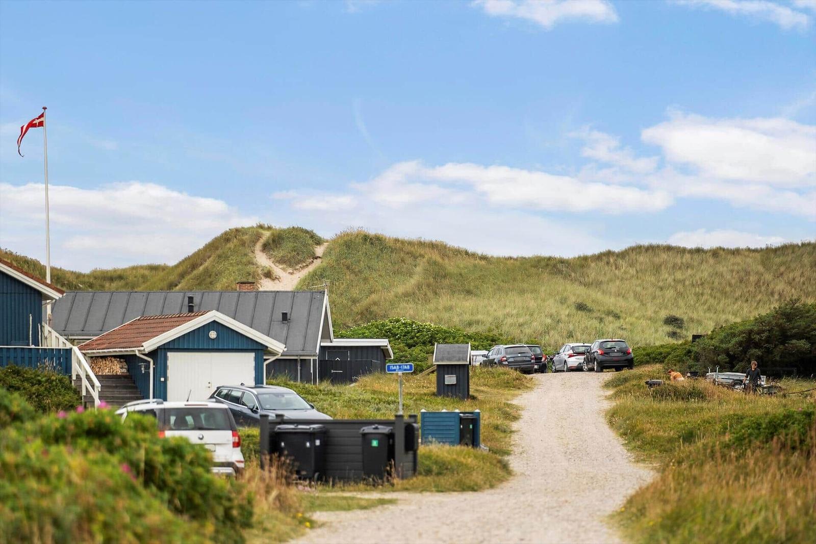 Dorfstraße mit Sanddünen und geparkten Autos unter blauem Himmel.