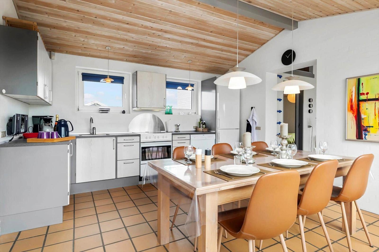 Küche und Essbereich mit Holzdecke, Tisch mit braunen Stühlen und Fenstern.