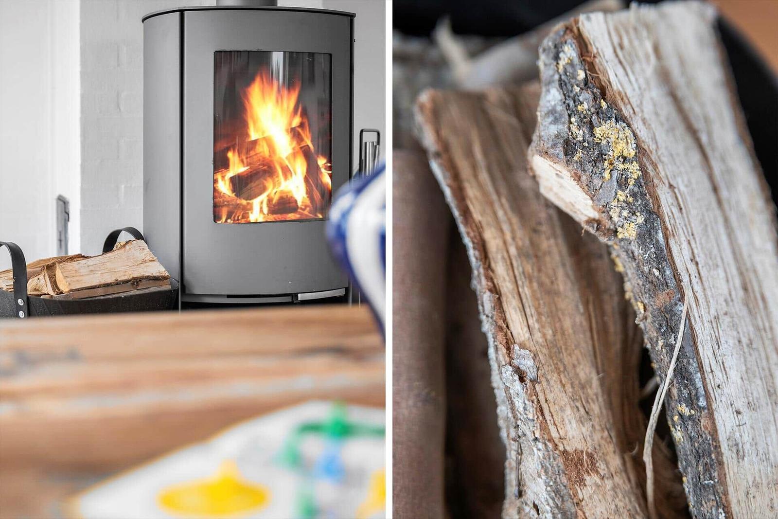 Moderne Holzofen mit brennendem Feuer und Brennholz im Hintergrund.