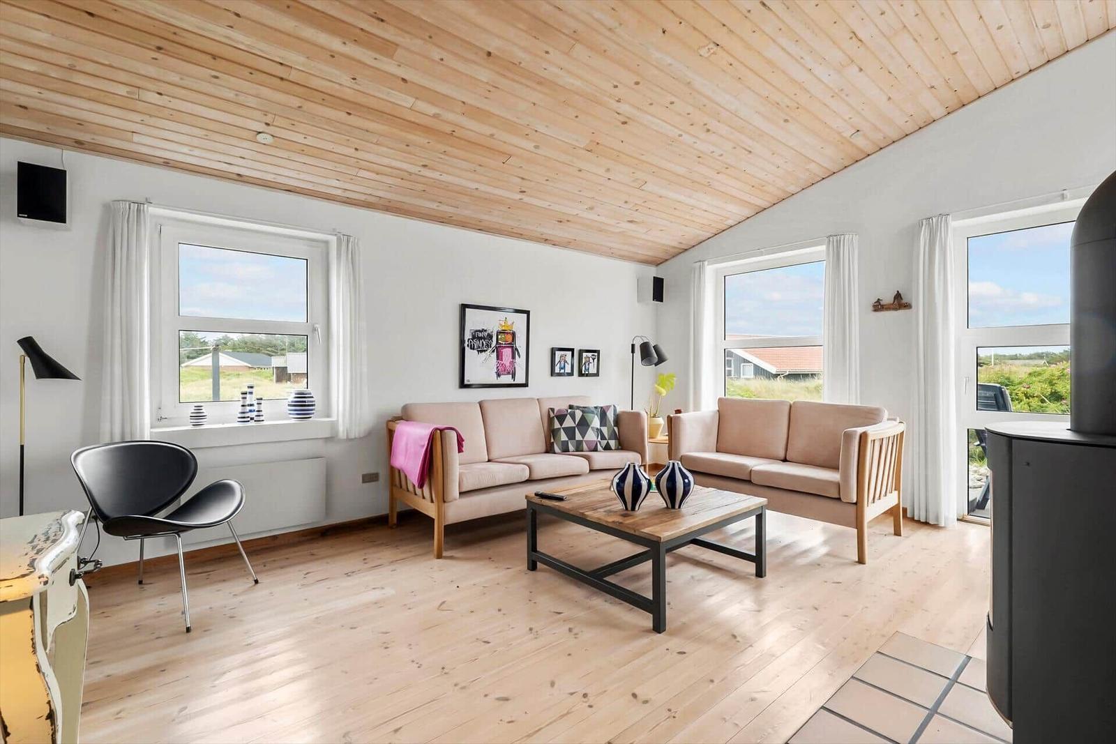 Wohnzimmer mit Holzdecke, zwei Sofas und großen Fenstern.