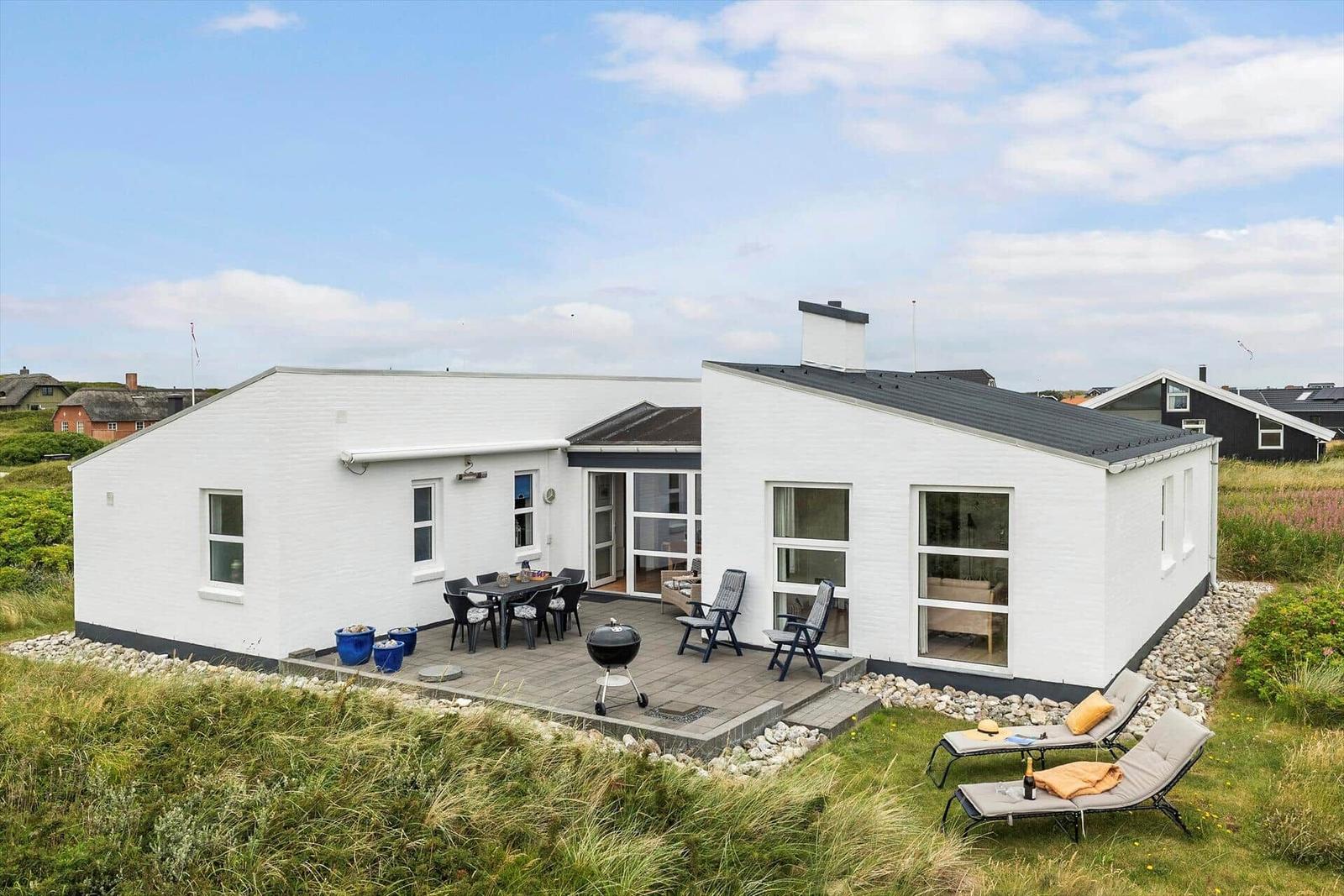 Weißes Haus mit Terrasse, Grill und Liegen im Gras.