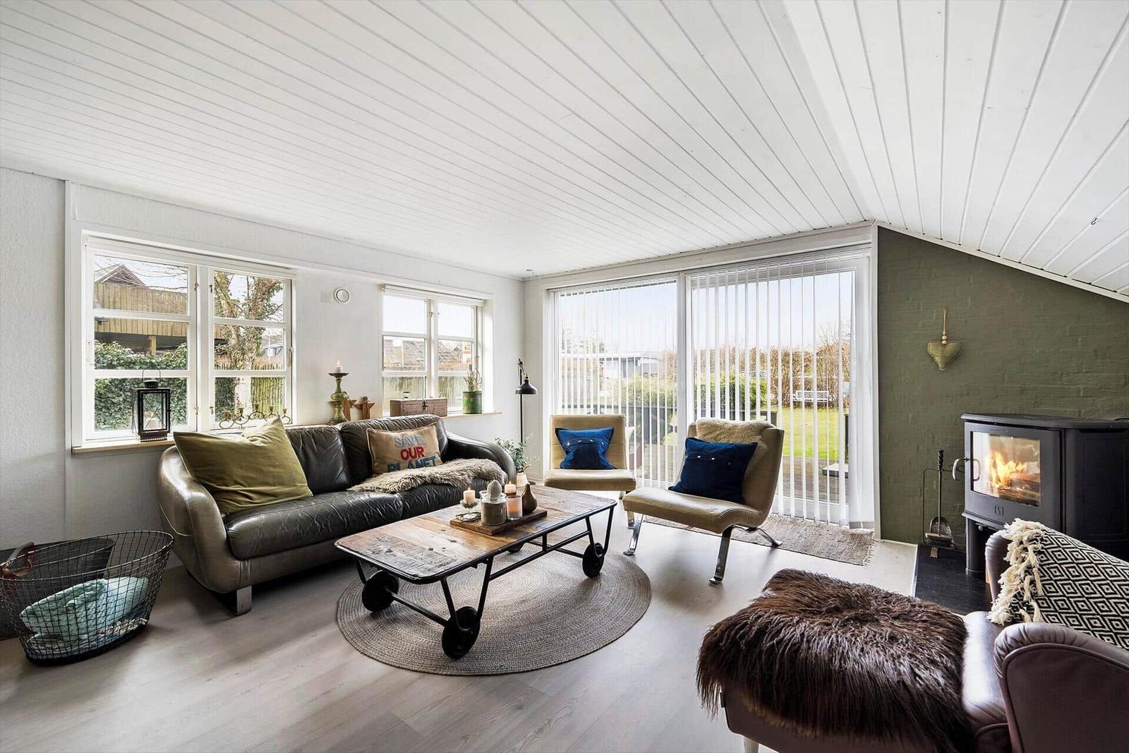 Wohnzimmer mit Sofa, Sesseln, Kamin und großen Fenstern.