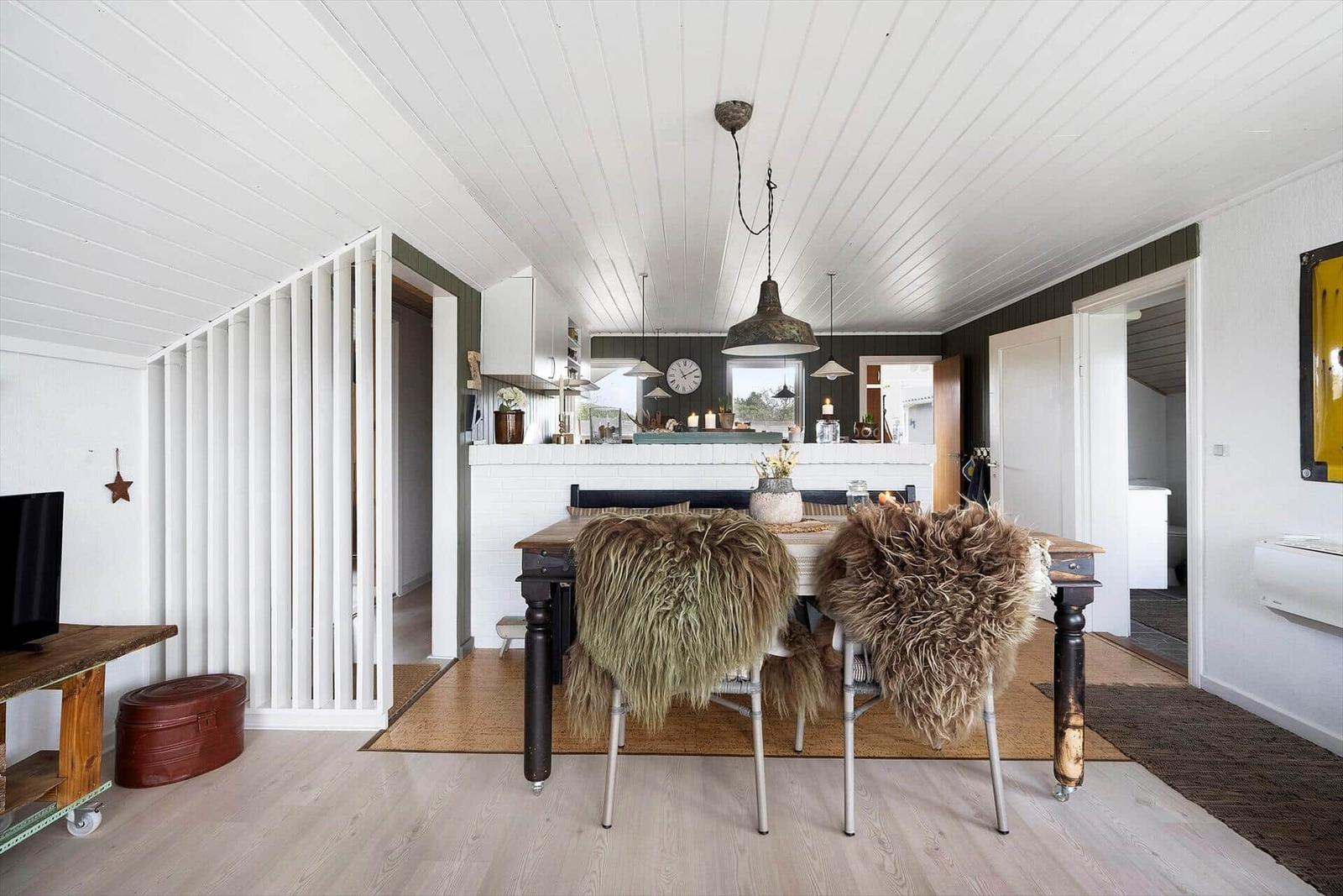 Esszimmer mit Holztisch, Fellbezogenen Stühlen und weißem Kachelwand im Hintergrund.