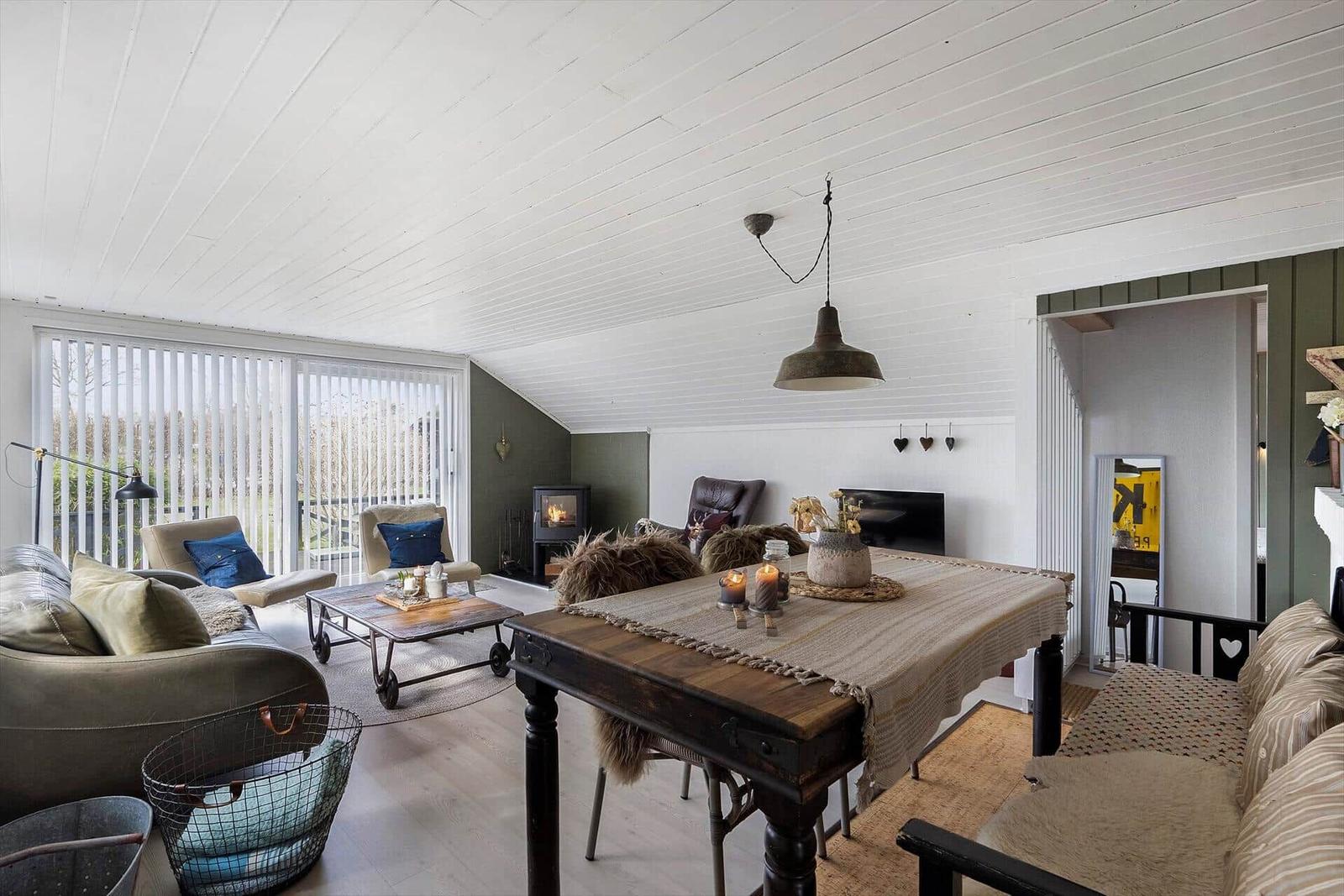 Wohn- und Essbereich mit Holztisch, Sofa und Kaminofen. Weiße Decke und Holzboden.