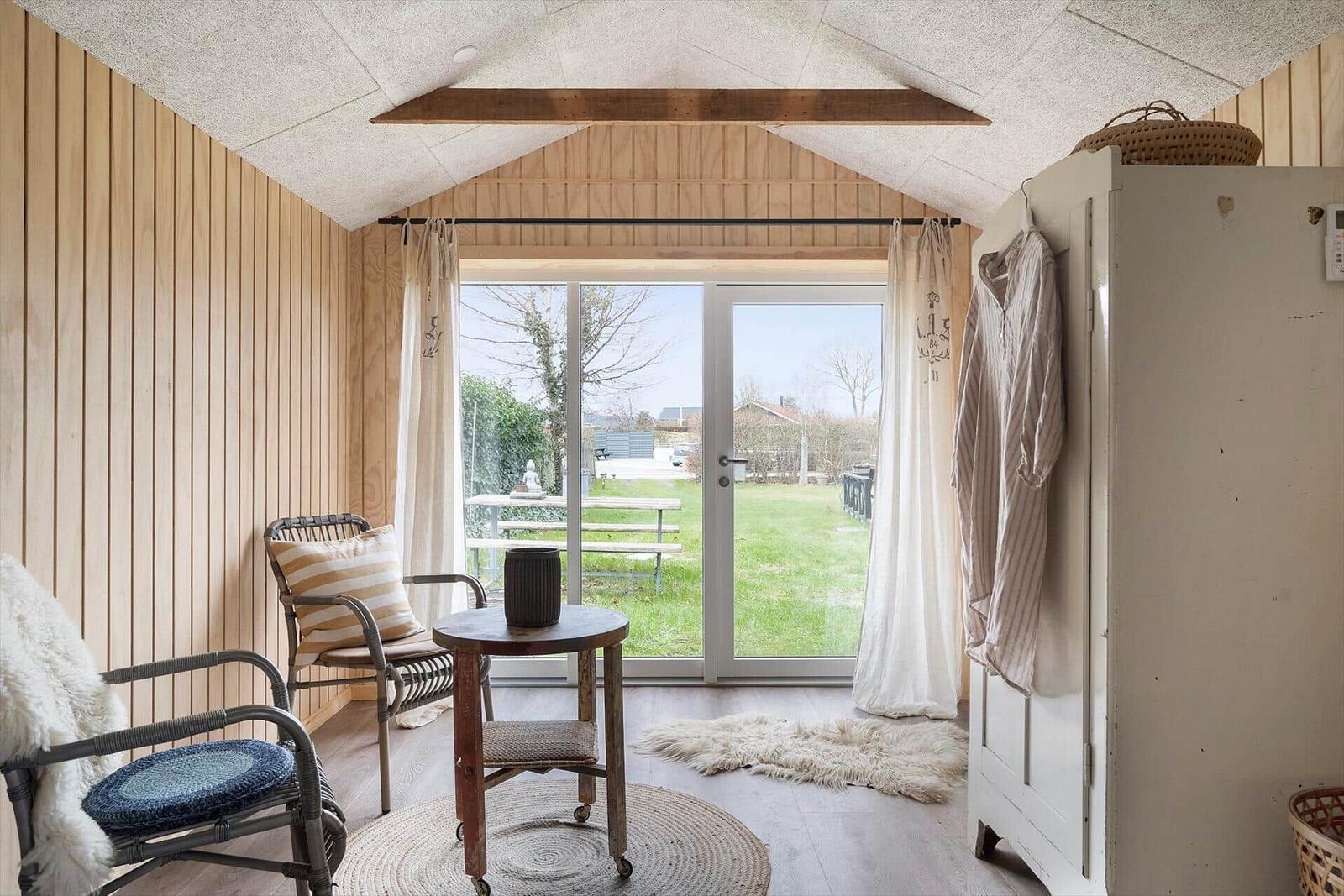 Raum mit Holzwand, Sitzgelegenheit und Glasfront zum Garten