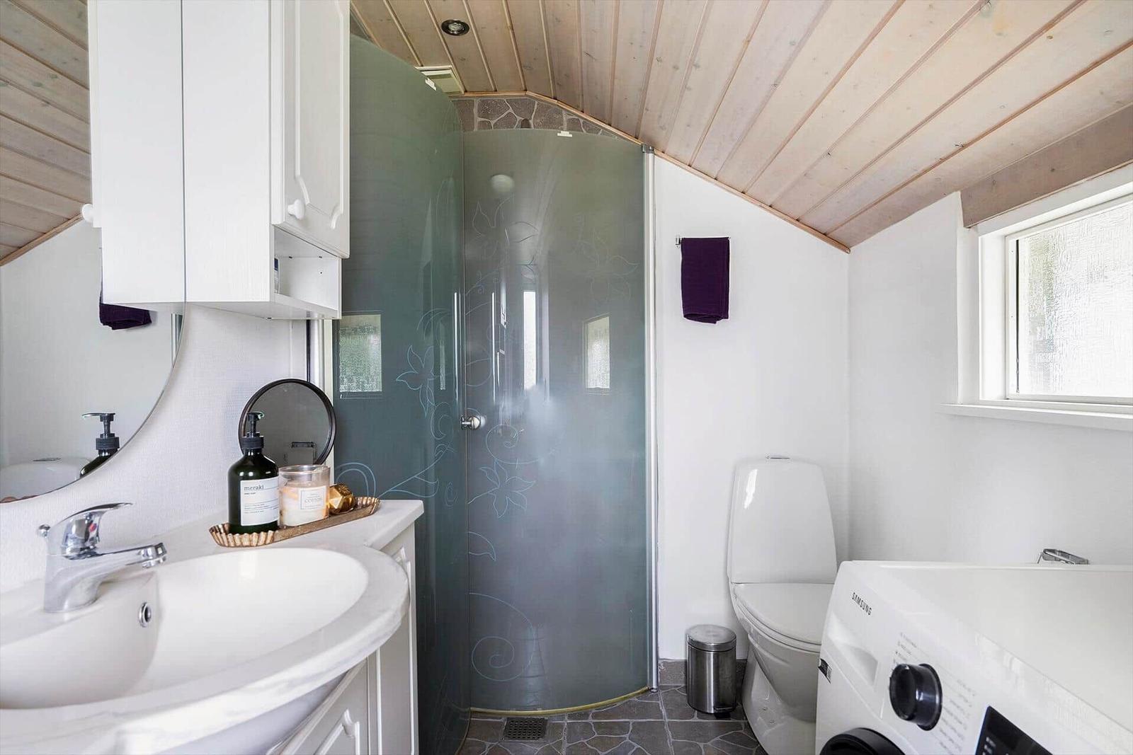 Badezimmer mit Dusche, Waschmaschine und Toilette unter Holzdecke.