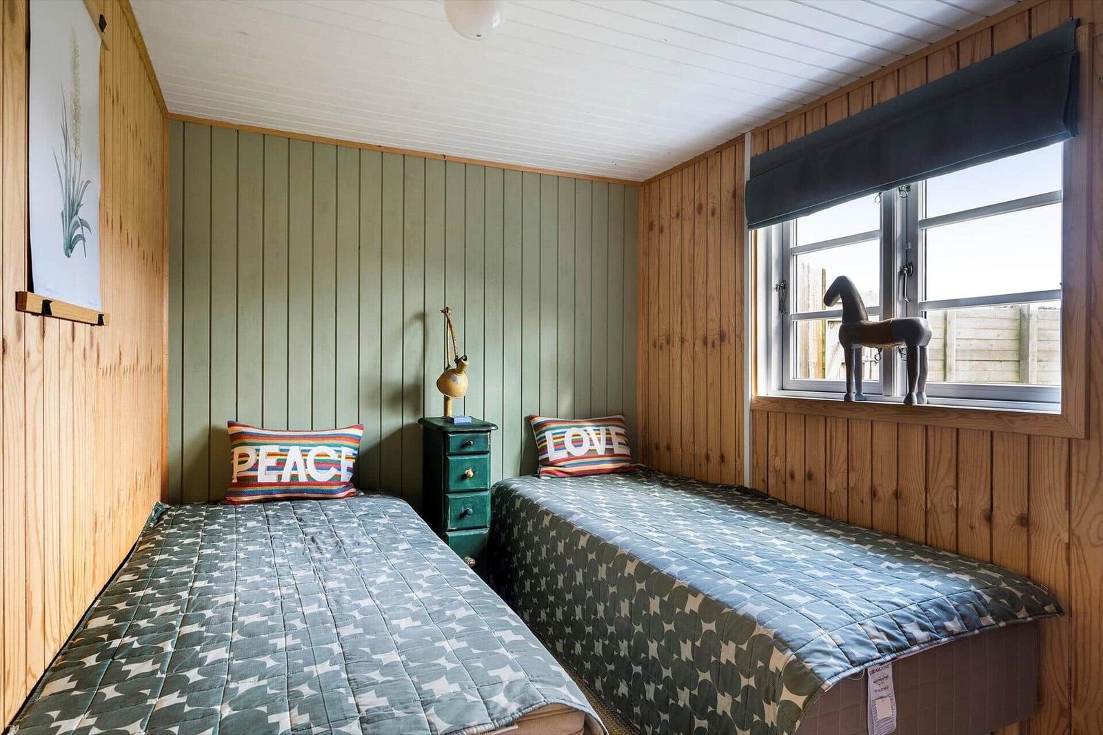 Zwei Betten mit gemusterten Decken, grüne Wand, Holzwände und Fenster mit Pferdfigur.