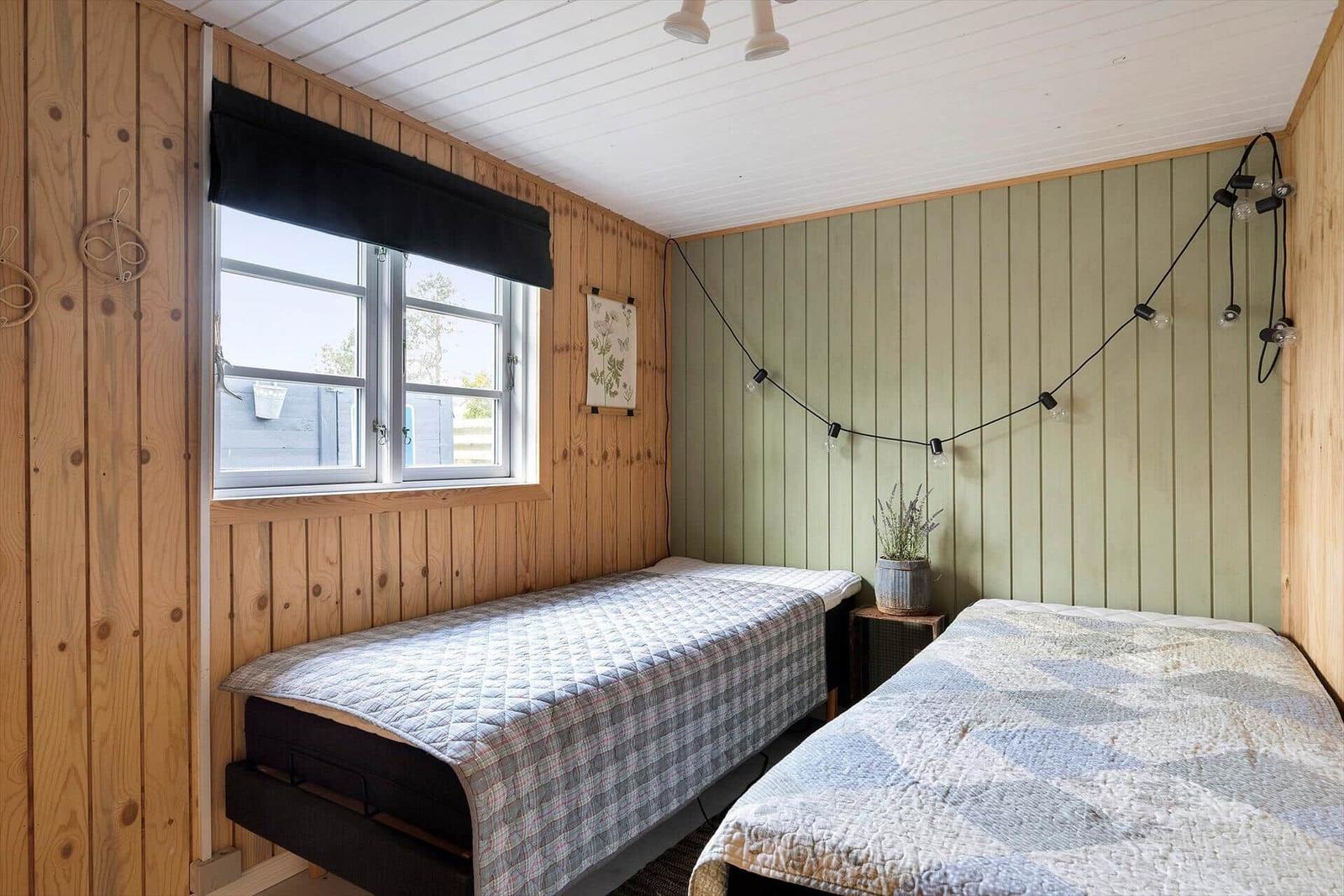Zwei Betten mit Quilt in einem Raum mit Holzwänden und Fenster.