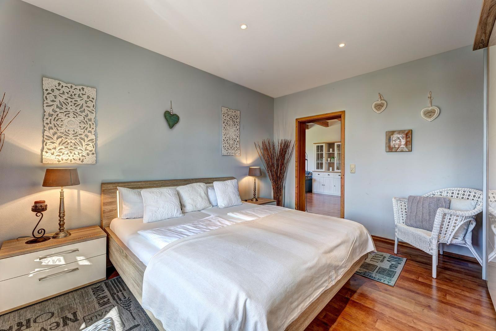 Bedroom with double bed, nightstands, and chair. Wooden floor and wall decor.