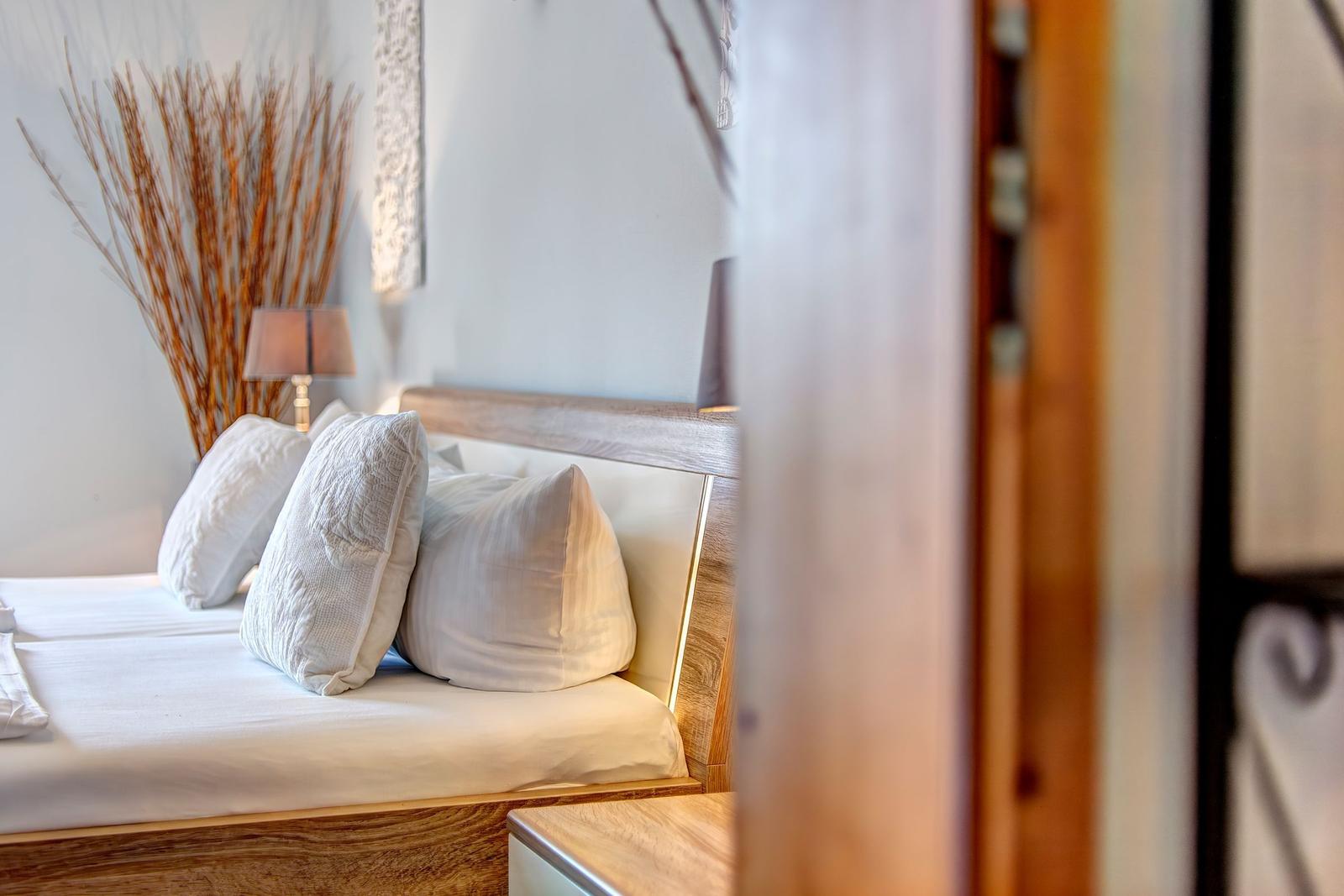 Bedroom with bed, pillows, and nightstand. Background with dried plants and wall decor.