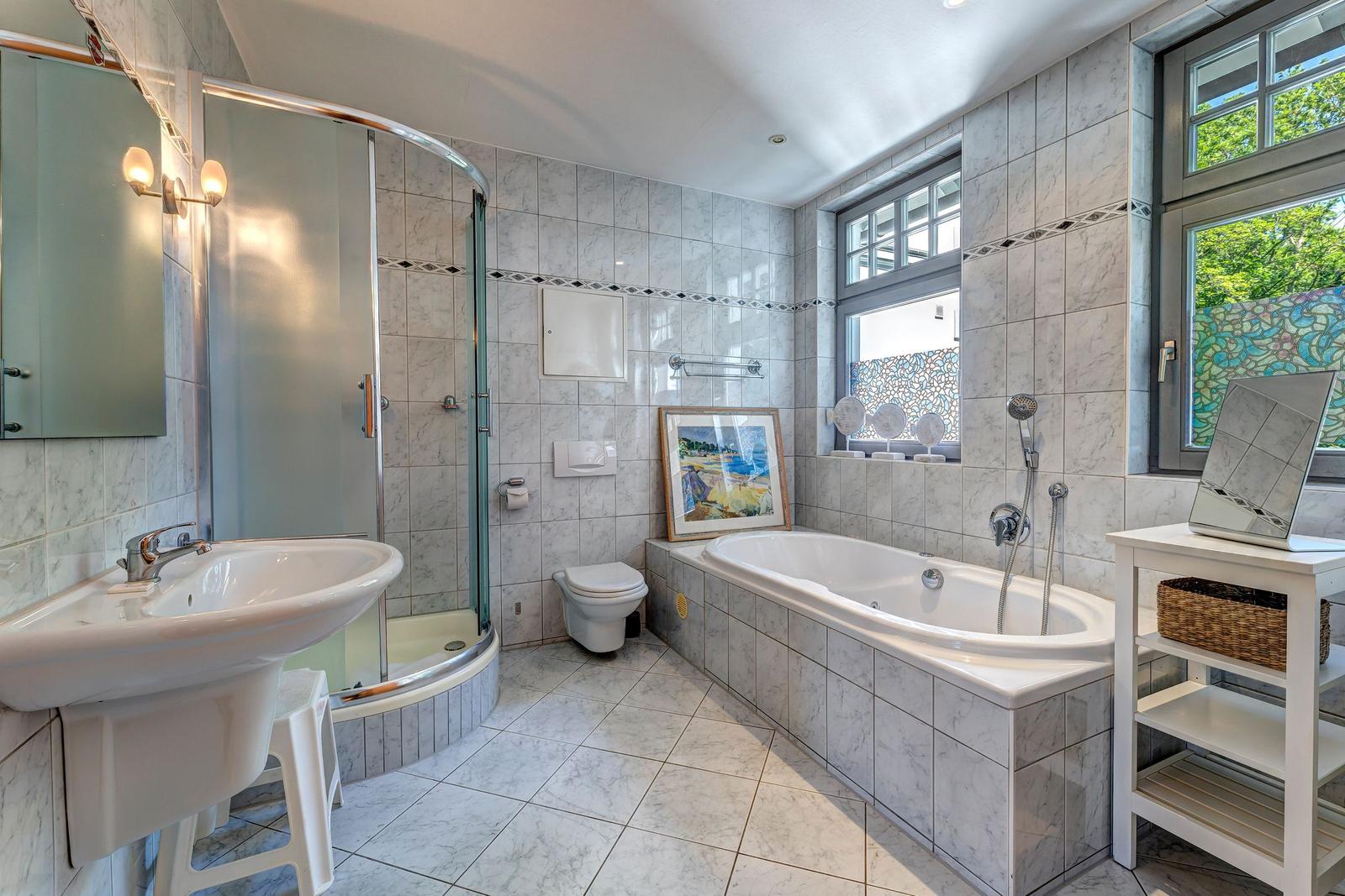 Bad mit Badewanne, Dusche, Waschbecken und Toilette. Fenster mit buntem Glas.