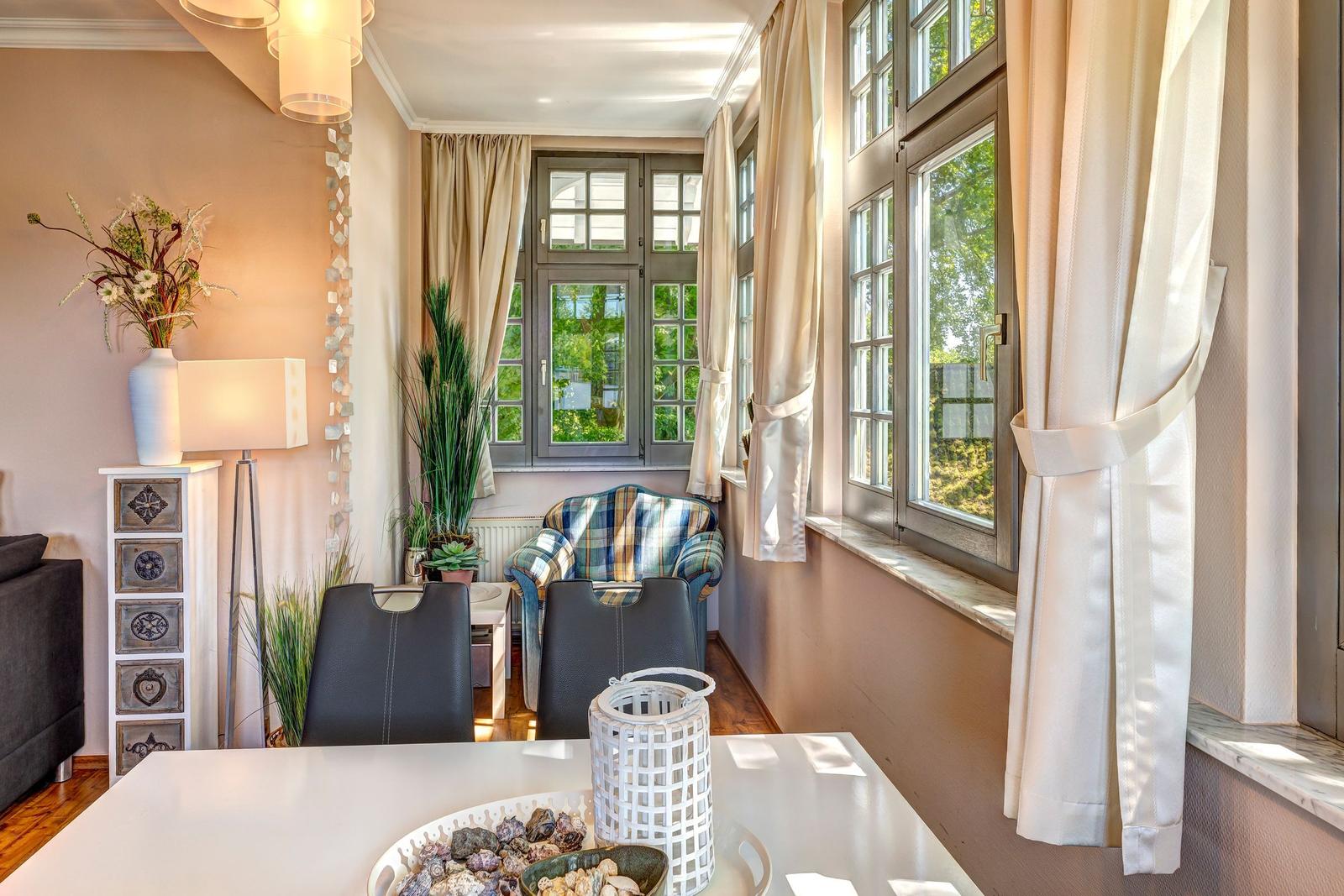 Essbereich mit Tisch, Stühlen und Fenstern mit Vorhängen.