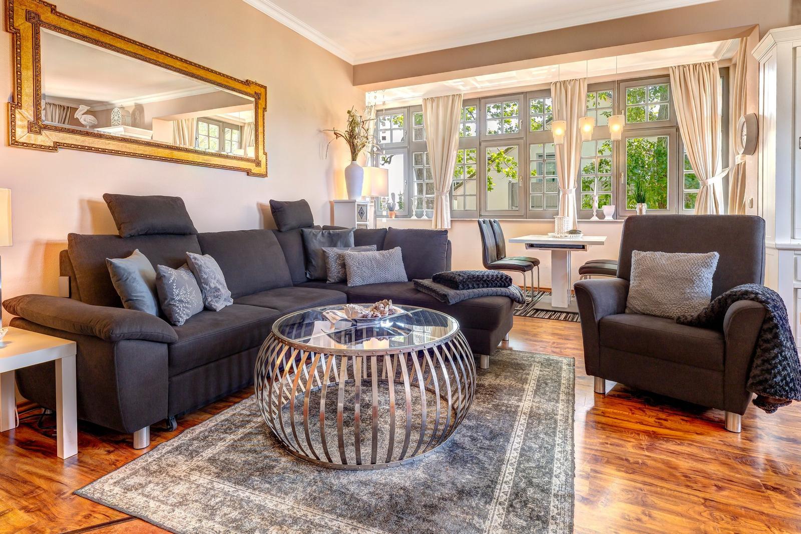 Wohnzimmer mit Sofa, Sessel und Glas-Tisch vor Fenster