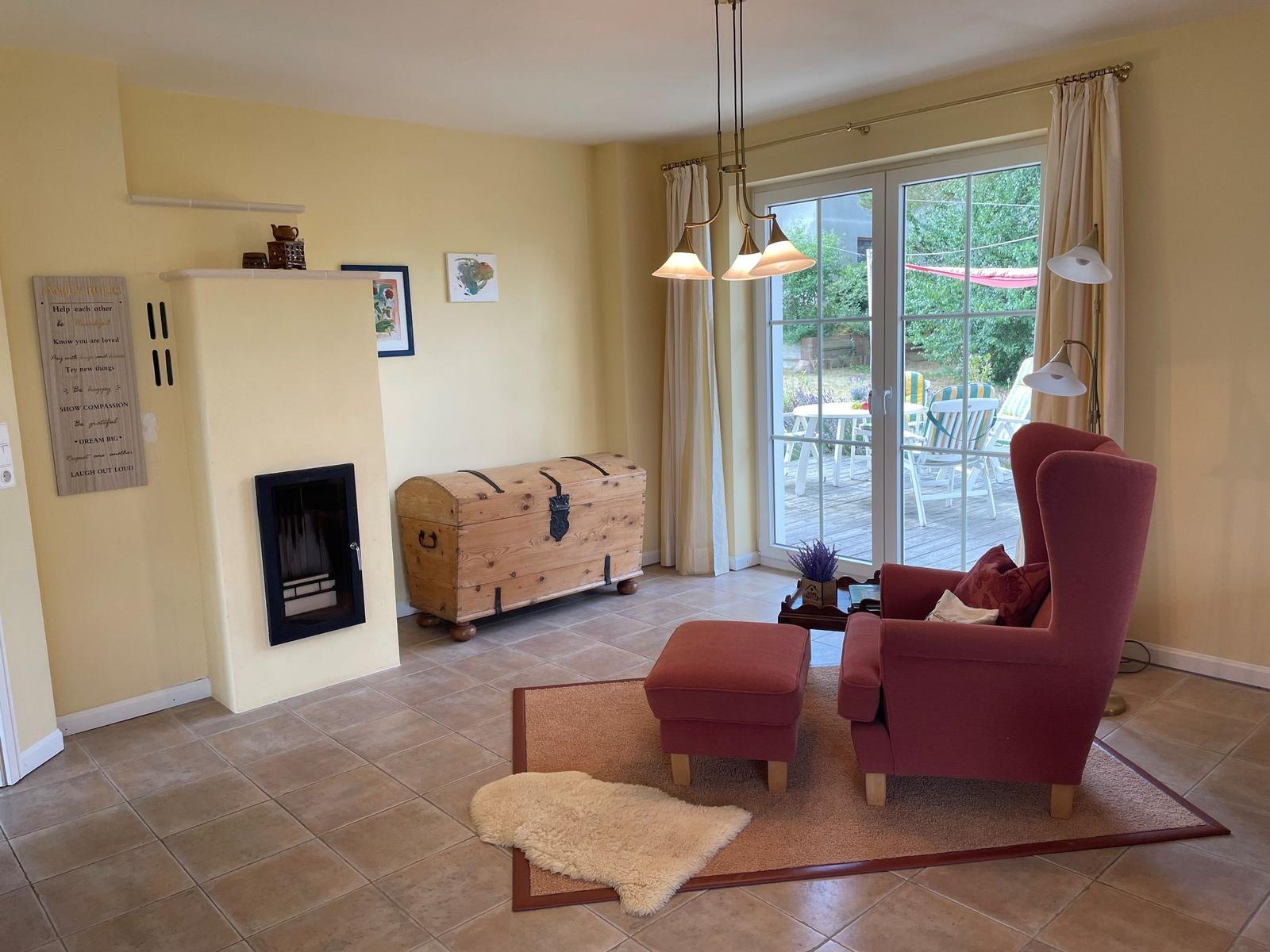 Wohnzimmer mit Sessel, Kamin und Terrasse. Holztruhe und Beleuchtung.