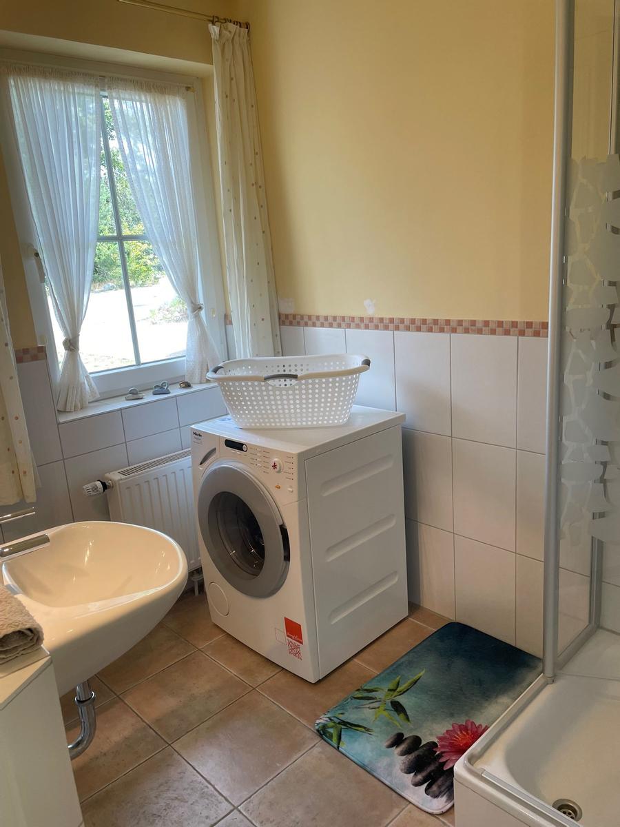 Badezimmer mit Waschmaschine, Dusche und Fenster mit Vorhängen.