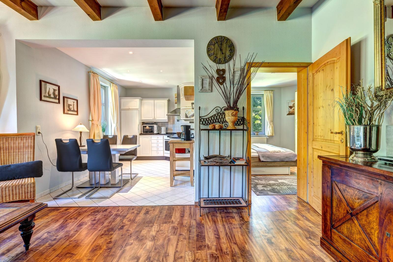 Wohnbereich mit Essbereich und Küche. Holzdielen und ein Schlafzimmer sind sichtbar.