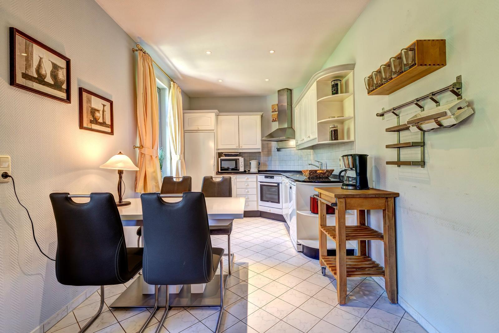 Küche mit Essbereich, weiße Schränke, Esstisch mit Stühlen und Küchenzeile.