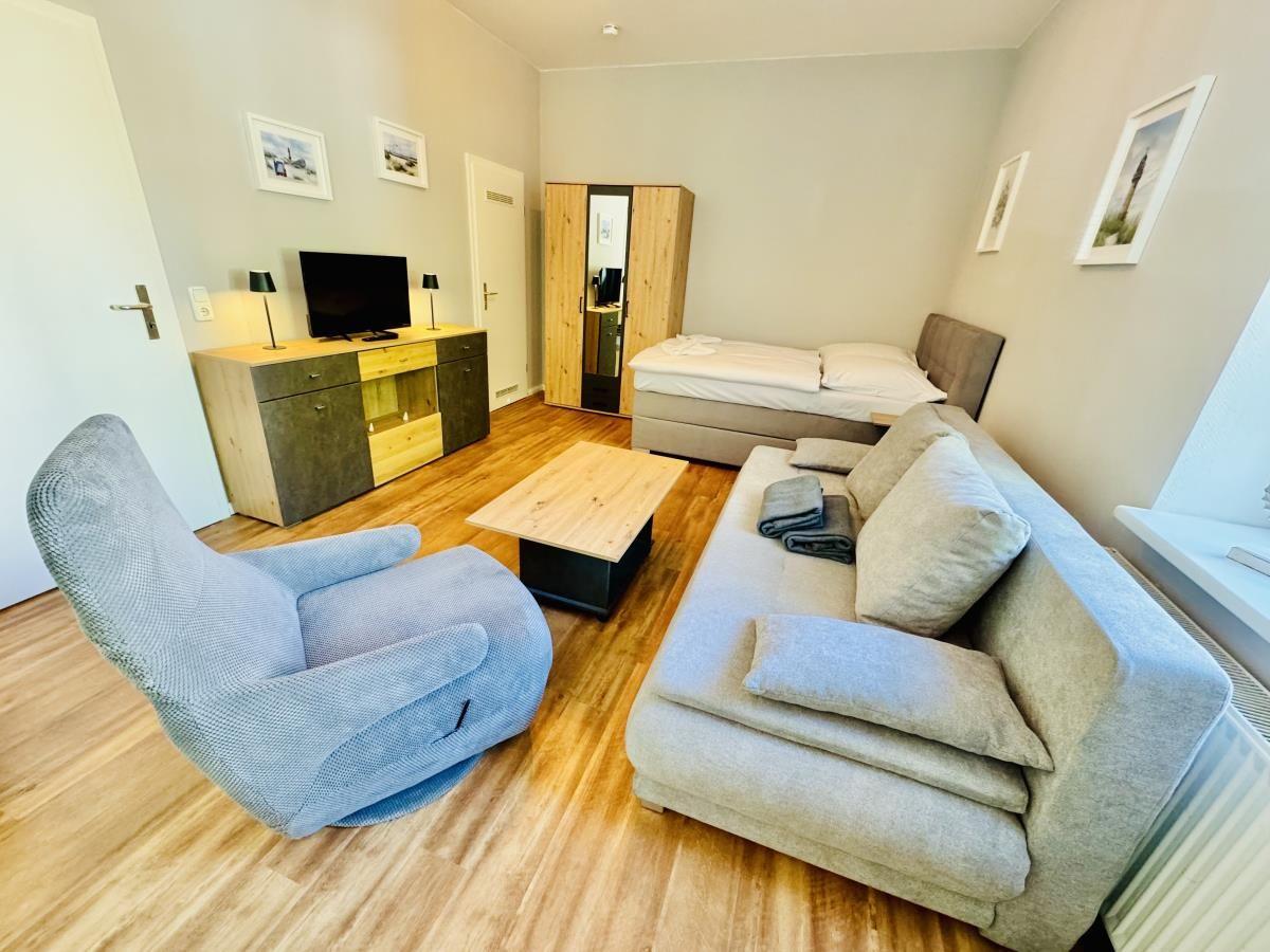 Wohnzimmer mit Sofa, Sessel, Bett und Fernseher.