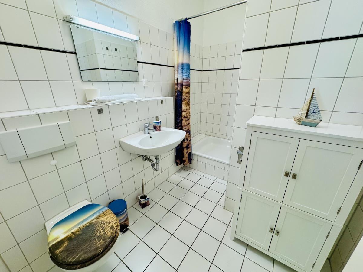 Badezimmer mit Badewanne, Waschbecken und WC. Weiße Fliesen und Schrank.