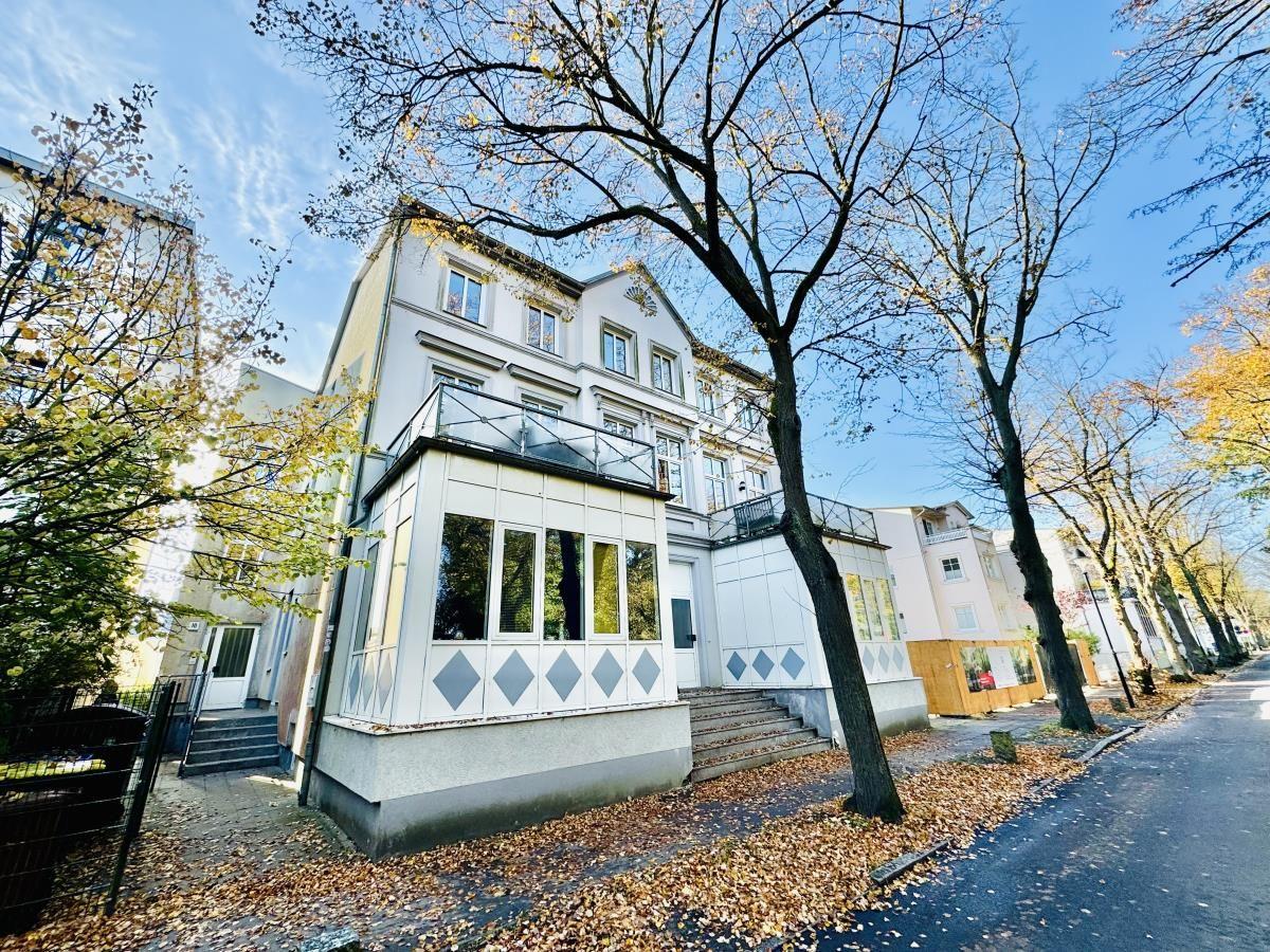 Modernes Haus mit Balkon und Treppenaufgang. Umgeben von Bäumen und Herbstlaub.