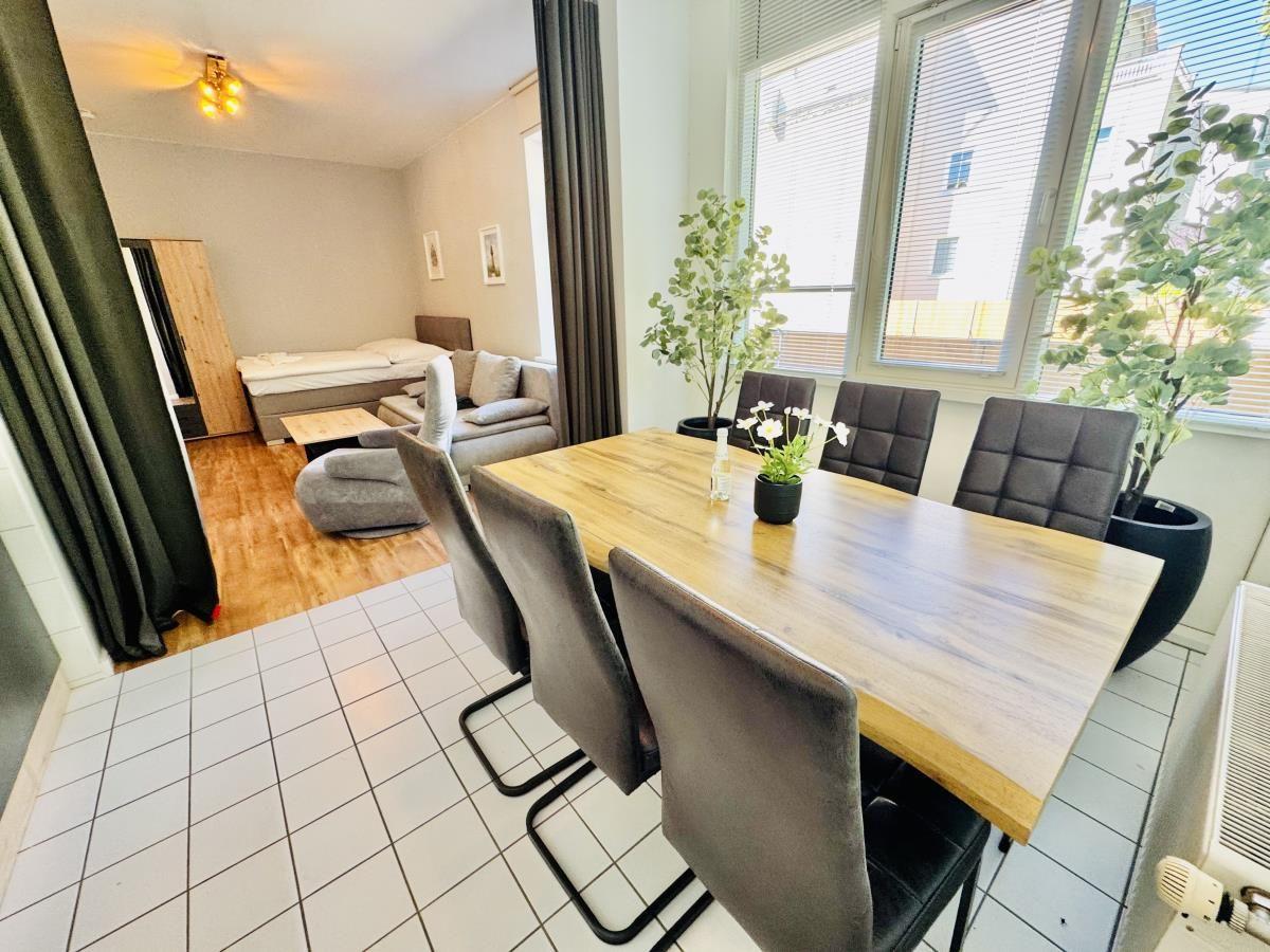 Essbereich mit Holztisch und Stühlen. Im Hintergrund Schlafzimmer mit Bett und Sofa.