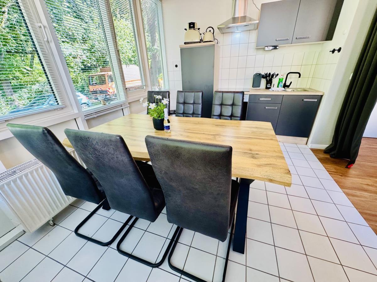 Essbereich mit Holztisch, vier Stühlen und Küchenzeile im Hintergrund.