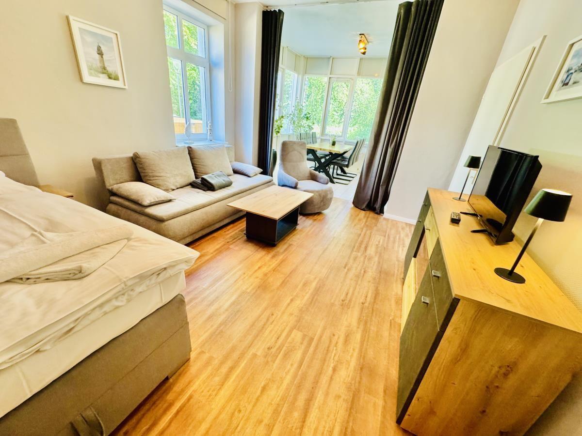 Wohnung mit Schlafzimmer, Wohnbereich und Essplatz. Holzboden und große Fenster.