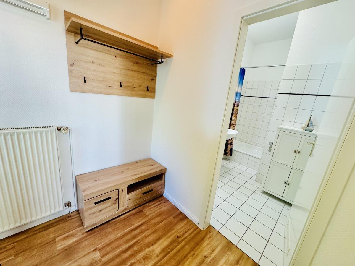 Flur mit Holzbank und Garderobe. Blick in die weiße Badewanne.