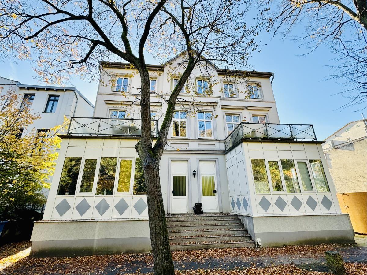 Ein zweistöckiges Haus mit Glasveranda und Stufen zur Eingangstür.