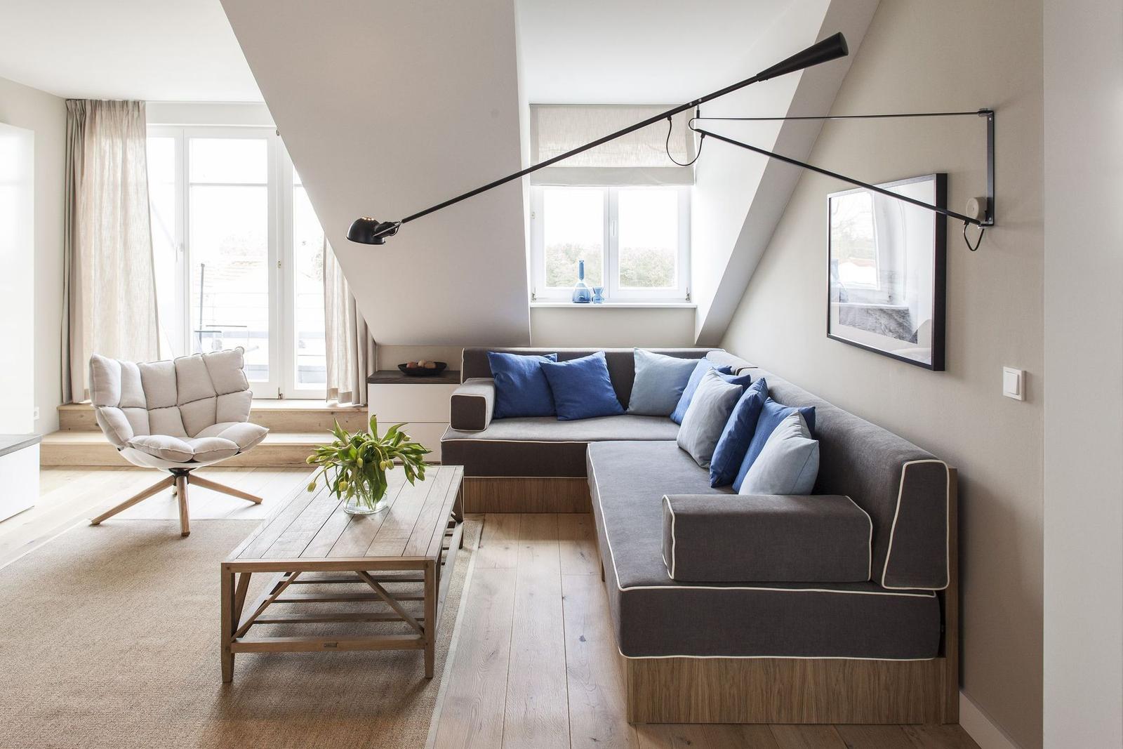 Wohnzimmer mit Ecksofa, Holztisch und Sessel unter Dachschrägen.