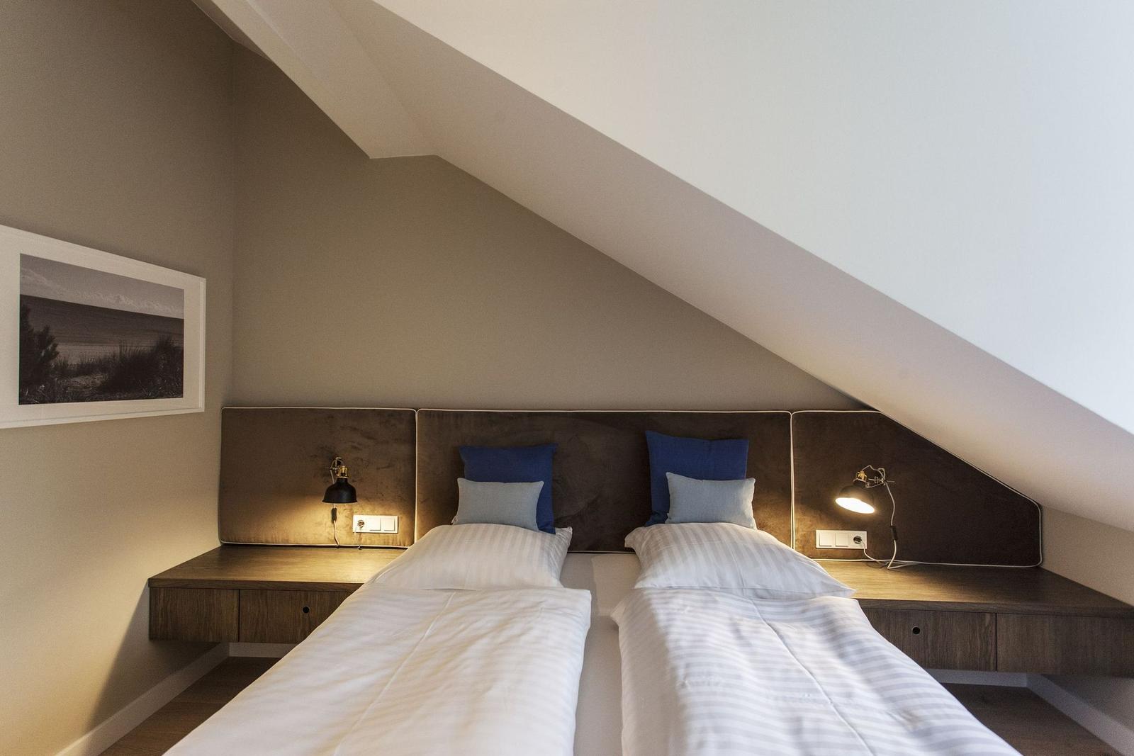 Zwei Einzelbetten unter Dachschräge mit Nachttisch und Wandbild.