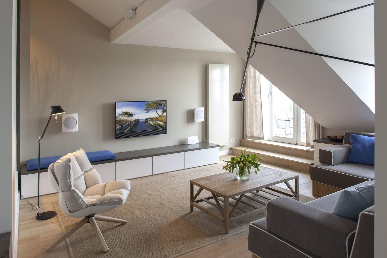 Wohnzimmer mit TV, Sofa, Sessel und Holztisch unter Dachschrägen.