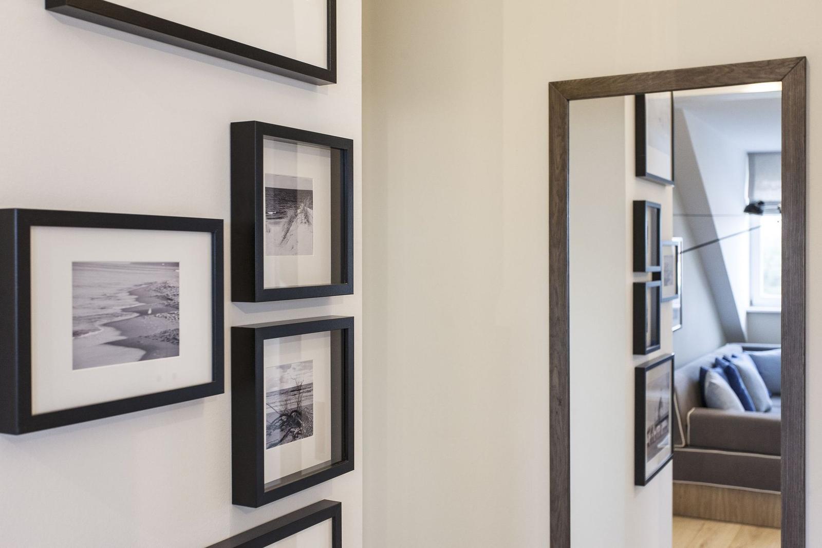 Wand mit schwarz gerahmten Bildern und Spiegel, der Wohnbereich reflektiert.