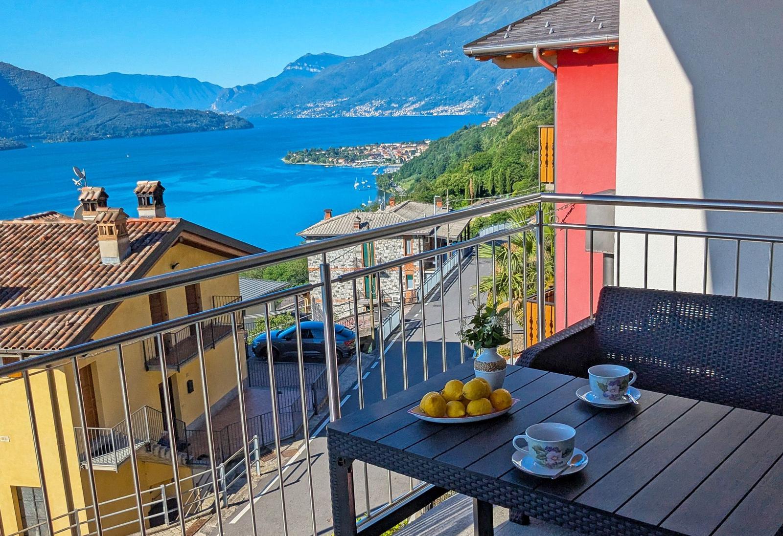 Terrasse mit Tisch, Stühlen und Blick auf See und Berge.