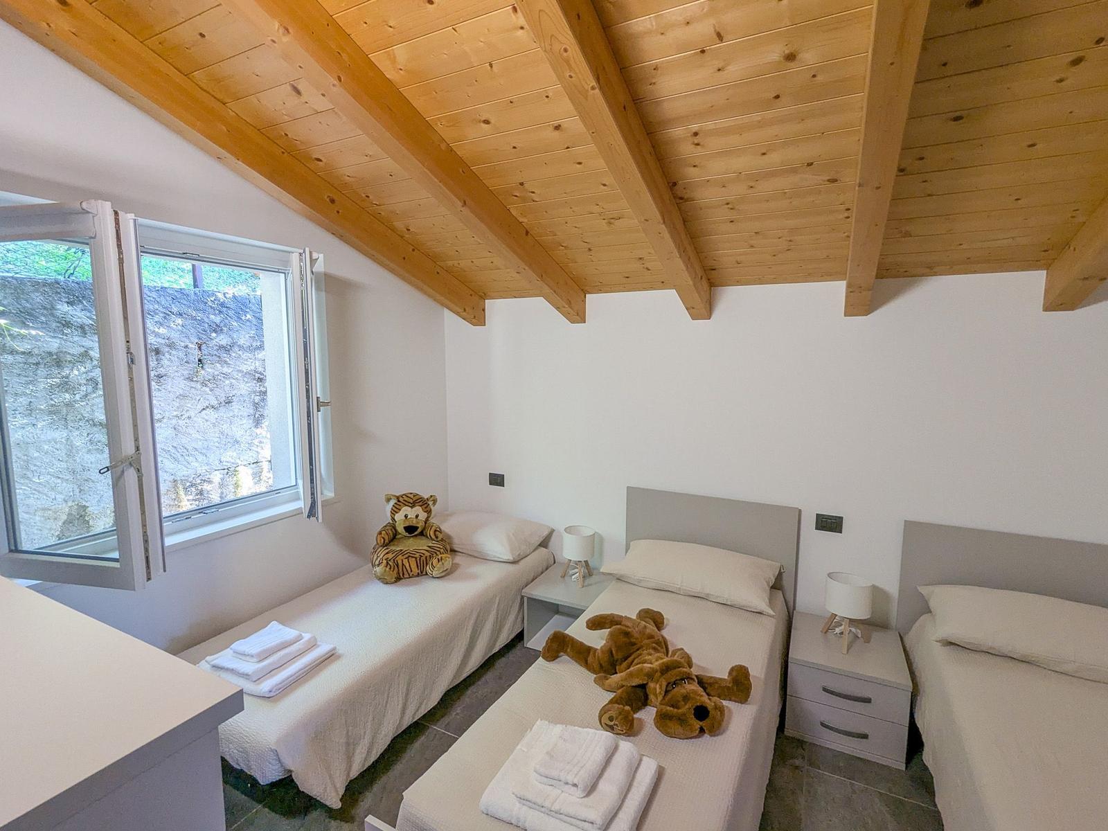 Zimmer mit drei Betten, Holzdecke und Fenster mit Blick auf Steinwand.